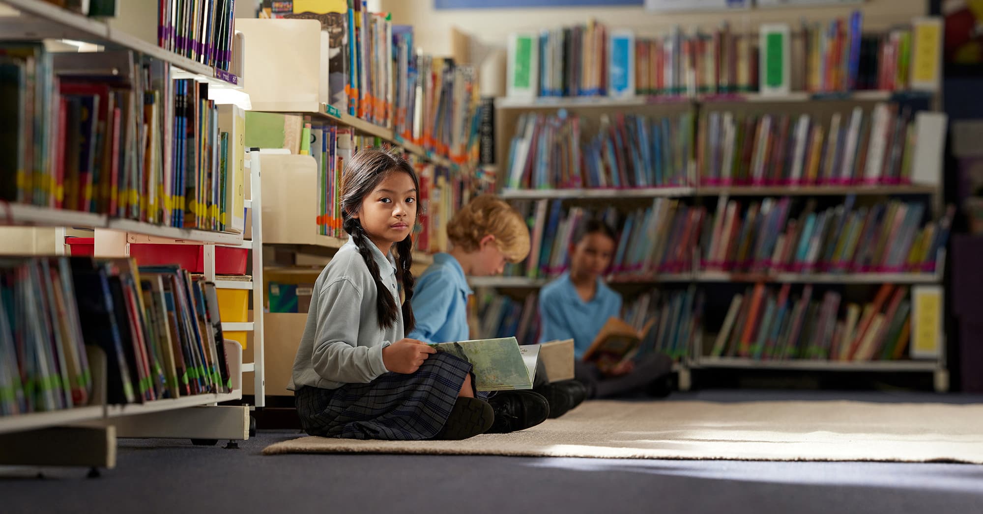 students sitting on the floor of the school library reading books