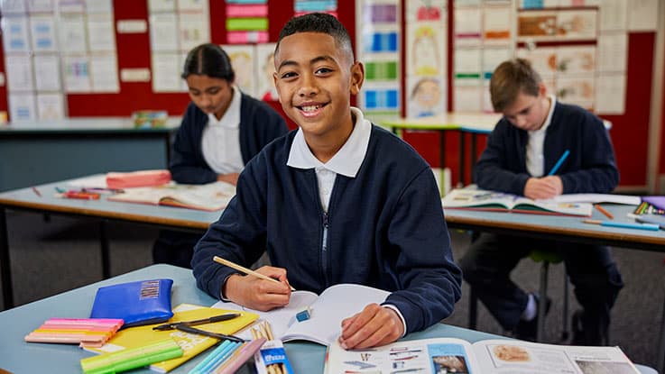 boy child at school desk with stationary smiling