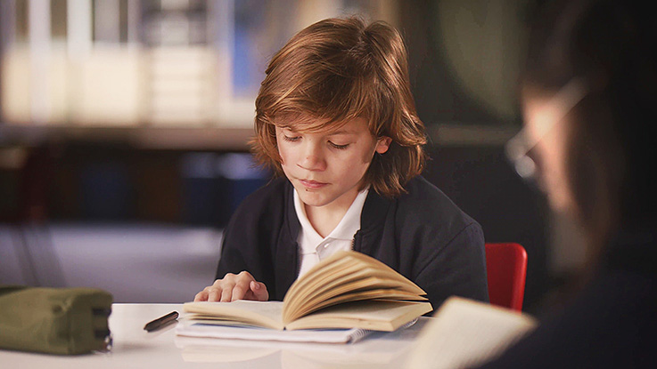 a school child is reading a book in a library
