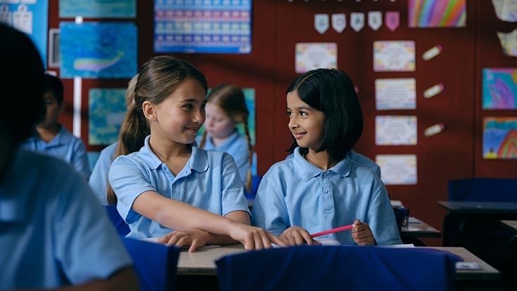 School girl sharing a desk with friend in classroom
