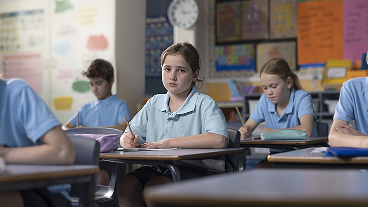 Girl sitting in classroom with other kids doing school work