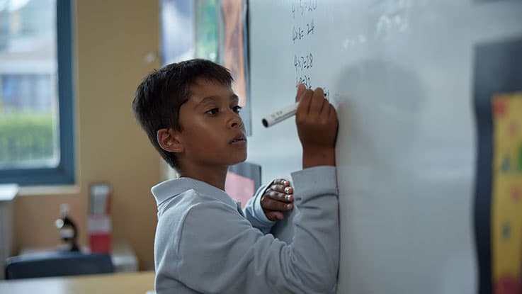 student working on maths work on whiteboard in classroom