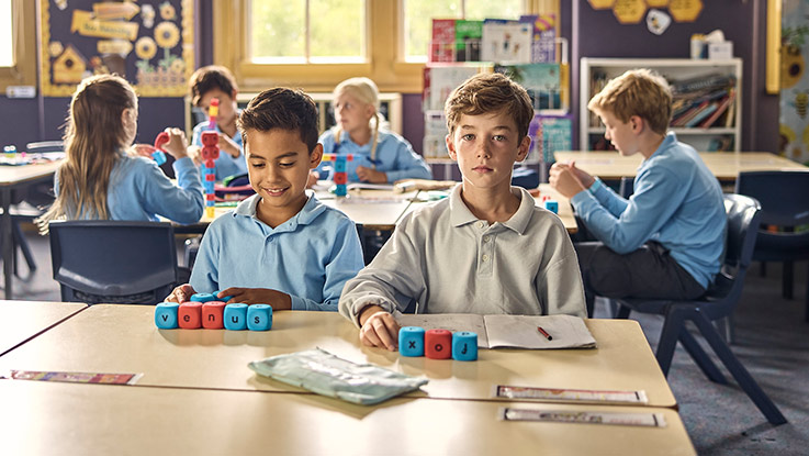 a school boy at his desk in the classroom looking directly at the camera surrounded by other students