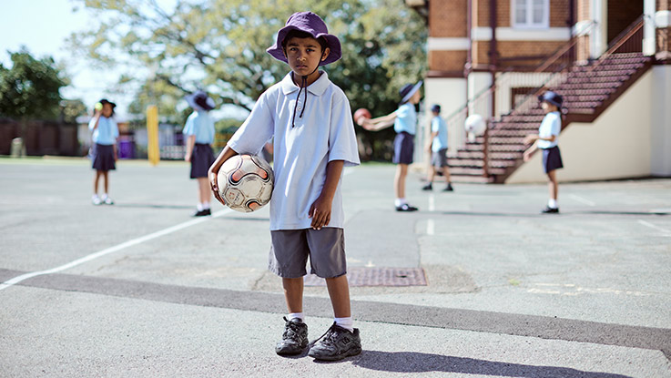 A school boy is standing alone in a playground