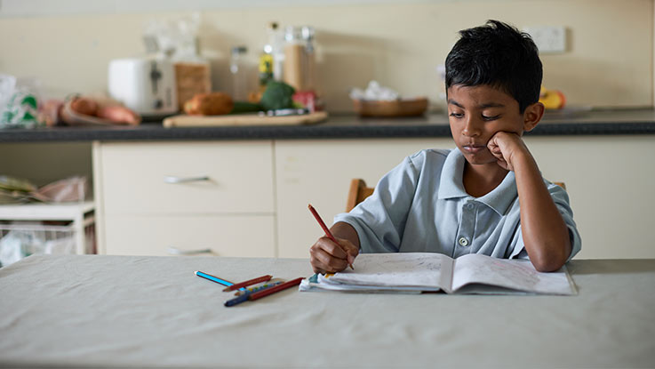 Boy sitting at kitchen table alone doing homework