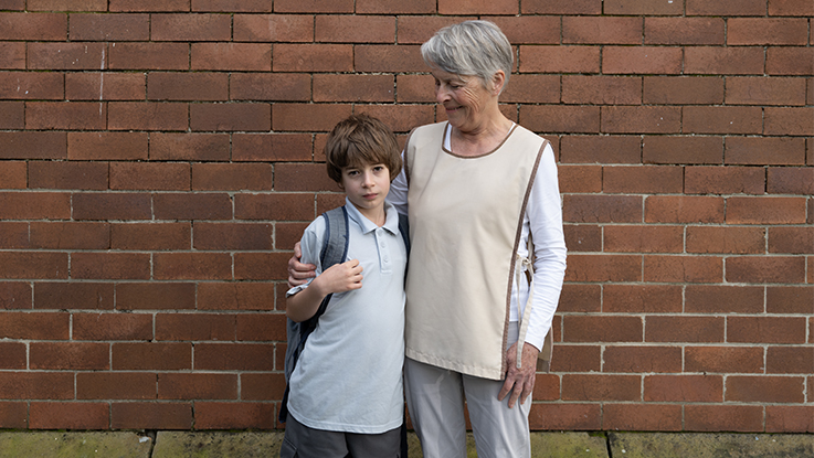 Boy and grandma standing in front of brick wall at school