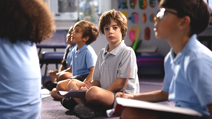 Group of young students sitting cross-legged on the classroom floor, listening attentively during a lesson.