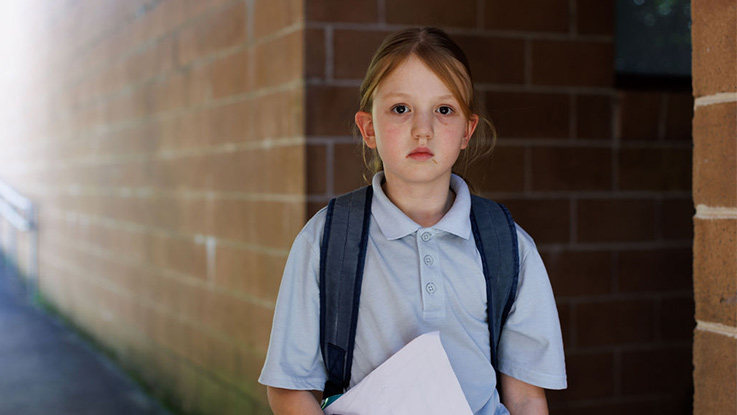 A school girl looking at camera holding a book