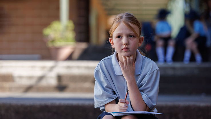 A school girl looking at camera completing a worksheet