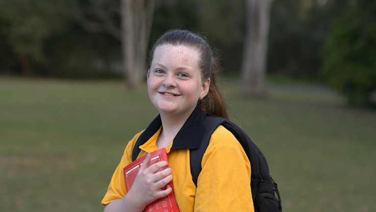 a young school girl holding her red book and carrying a backpack