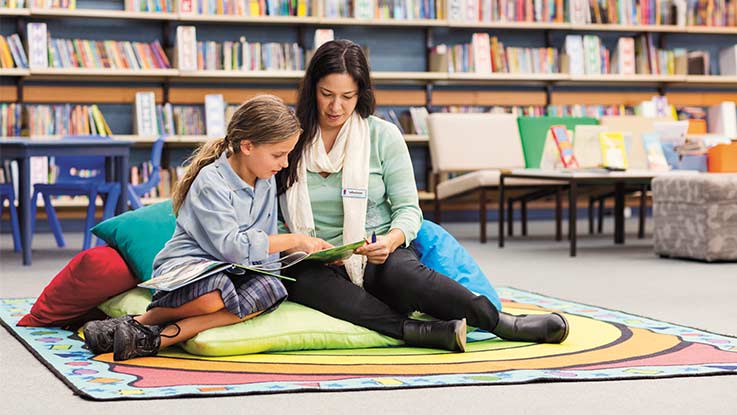 Mentor and girl sitting on library floor