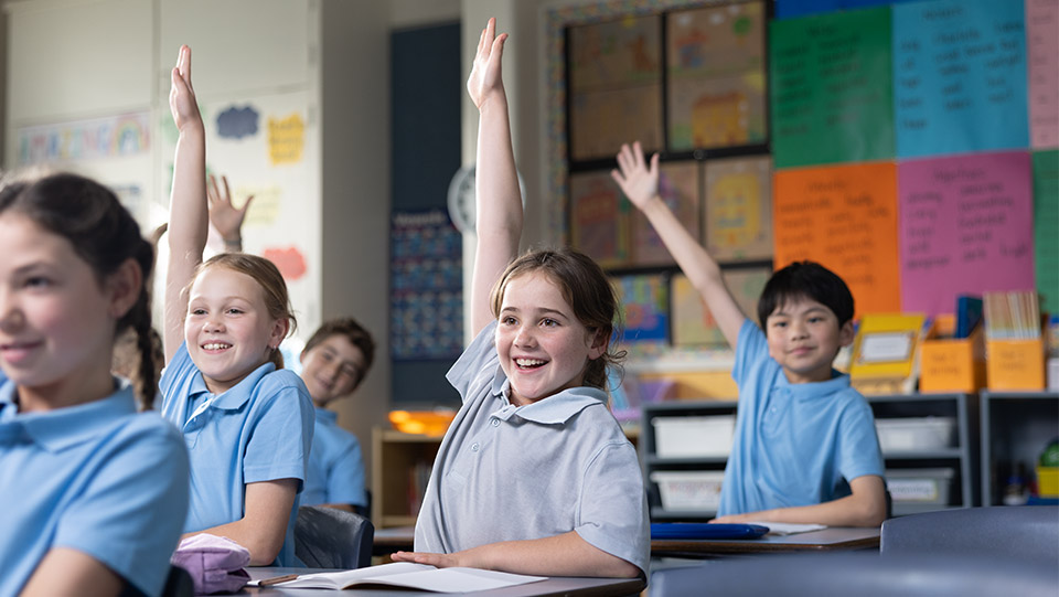 a school girl in a classroom with her hand up with other school students