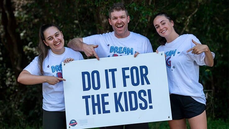 Three adults holding a sign that says 'Do it for the Kids'.