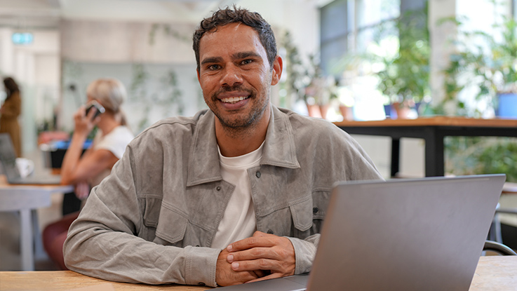 Man working on laptop smiling at camera in a work-place