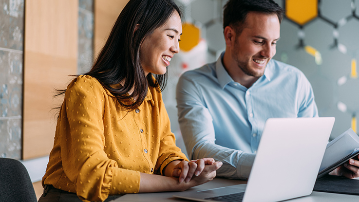 Two professionals working together on a laptop smiling