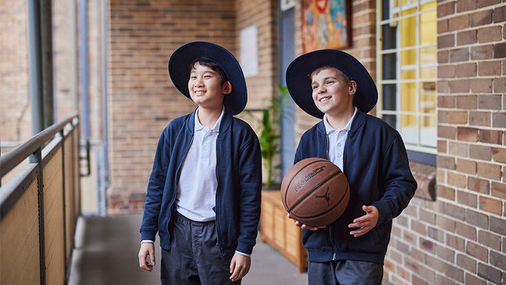 two school boys smiling at school while one is holding a basketball