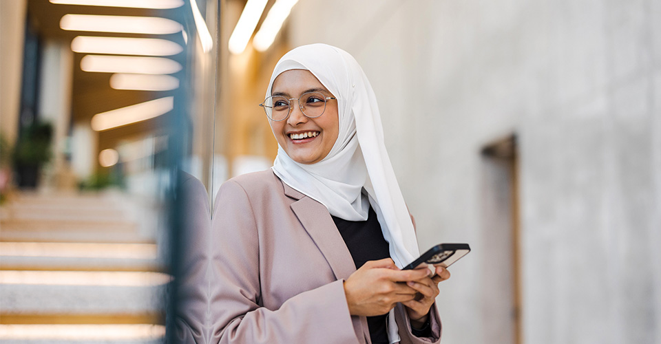 woman wearing a head scarf smiling and on her phone