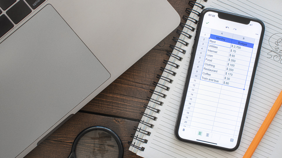 mobile phone showing a list of expenses on a notebook with a pencil next to it