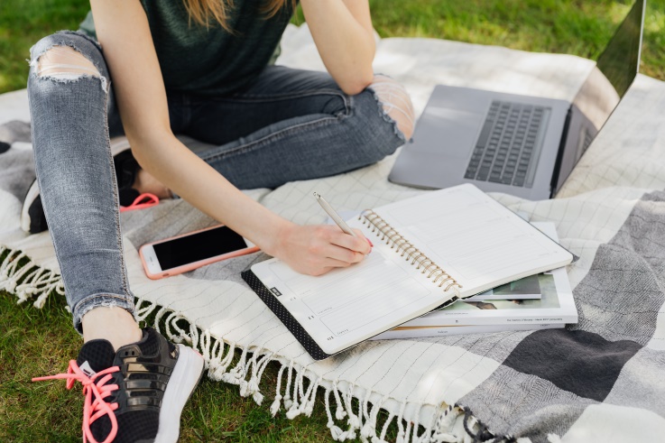 young girl taking notes in the park with a laptop