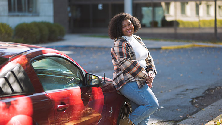 a woman standing in front of her red car