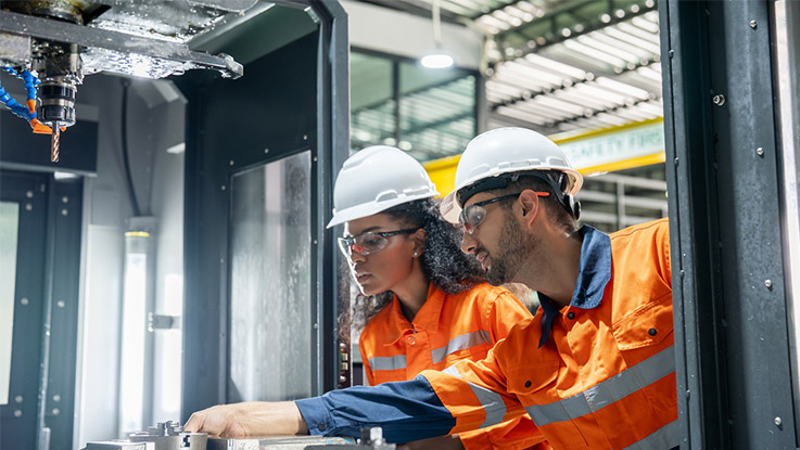 two engineers wearing orange safety clothing and safety hat pointing at an object