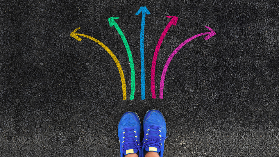 person with blue shoes standing before a set of arrows all different colours that are pointing different ways