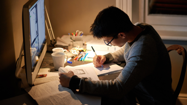 boy wearing glasses studying at their computer desk at night