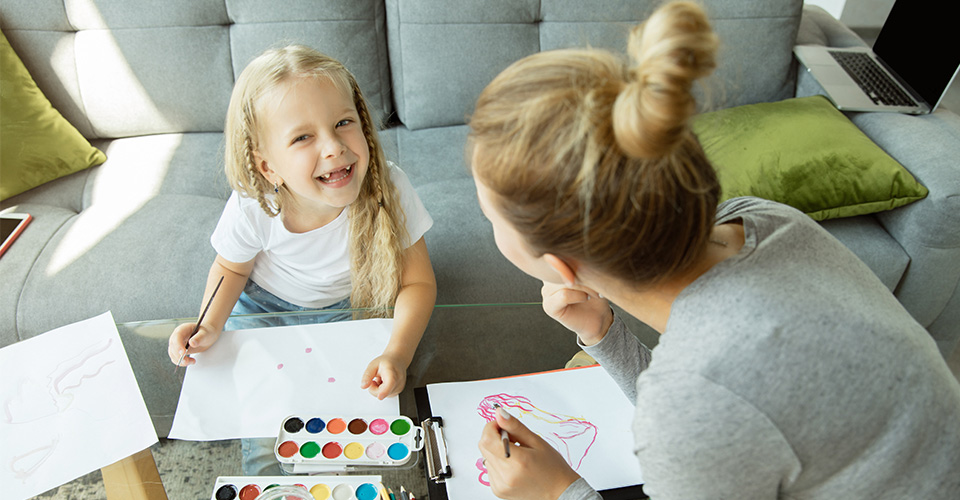 a young girl smiling and painting watercolours with her parent