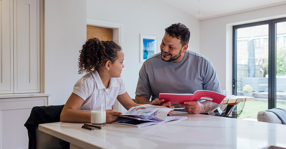 a young girl sitting at the kitchen bench with her father looking at each other while reading