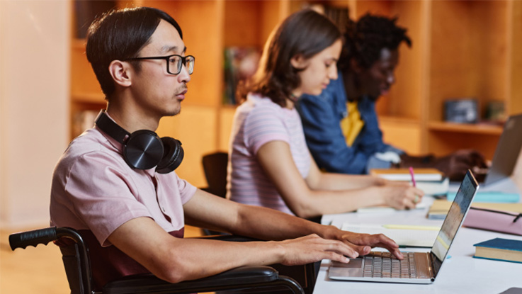disabled student studying at their laptop at the desk with other students