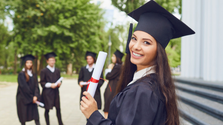 Student holding a graduation certificate and smiling in graduation cap and gown.