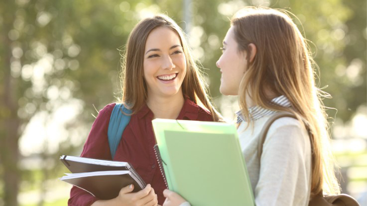 Two women chatting outside while holding folders