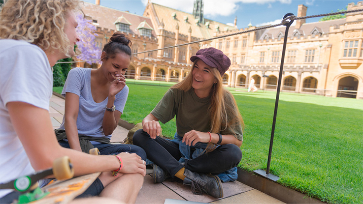 Students sitting on grass outside a university building talking and studying together.