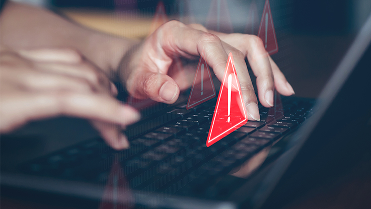 Hands typing on a laptop keyboard with digital warning icons representing online security threats or cyber risk.
