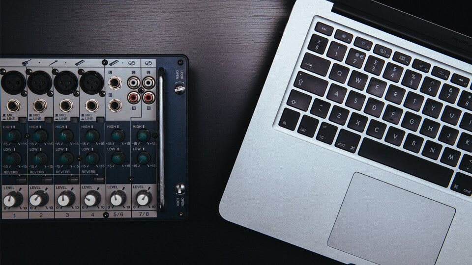 A top-down image of a laptop and an audio mixer on top of a desk