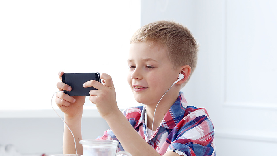 A young boy is watching his phone and wearing in-ear headphones