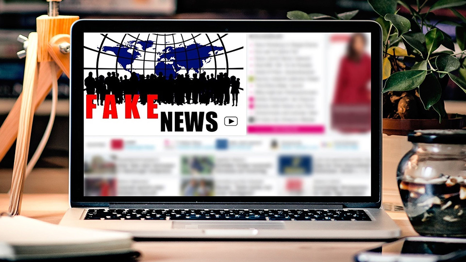A laptop sitting on a table with an article blurred out and 'fake news' titled over the top