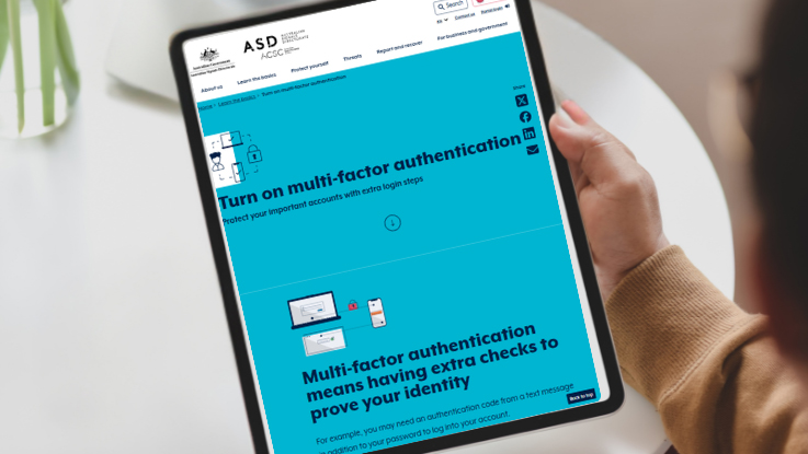 A person holding a mobile phone displaying a webpage about multi-factor authentication and protecting online accounts from identity theft.