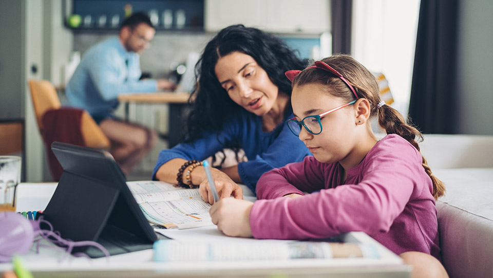 a parent is helping their daughter with school work with tablet in front. the father is sitting in the foreground