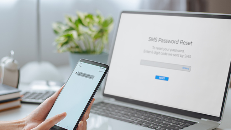 Person holding a smartphone near a laptop displaying a login or account verification screen, representing online account security and authentication.
