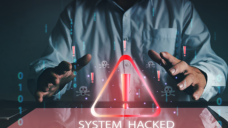 Hooded hacker using a laptop with glowing red warning triangle and cybersecurity threat concept.