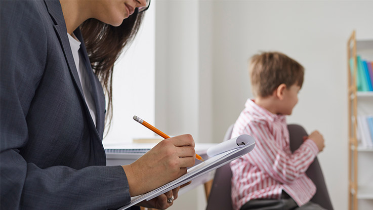 a therapist is taking notes while a child is playing