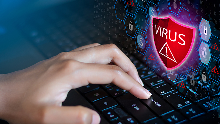 Hands typing on a laptop keyboard with a digital virus warning shield representing malware, cybersecurity threats and online protection.