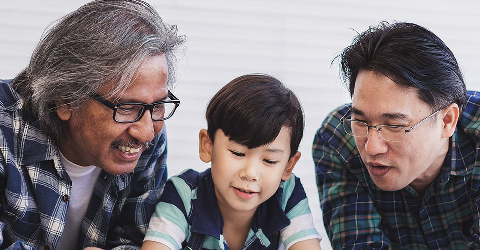 an older man with a young child and middle aged man circling around two smartphones together
