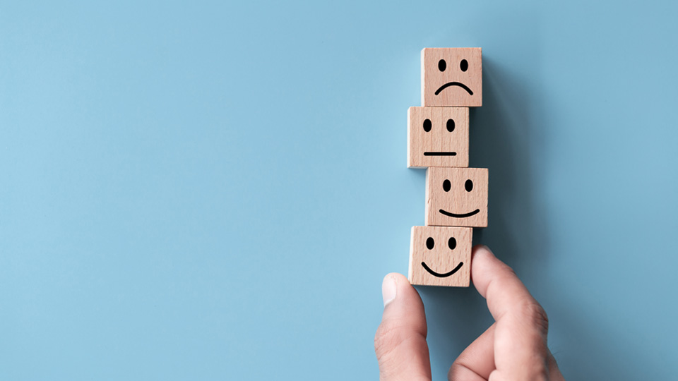 hand moving wooden blocks that have different emotions on them on a blue background