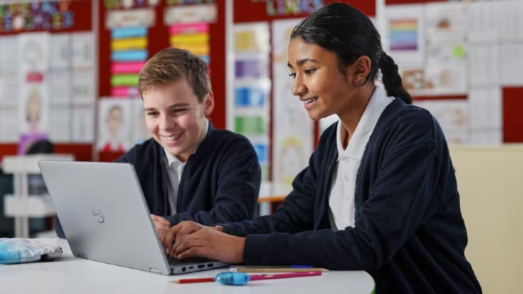 A young girl and boy use a laptop in the classroom.