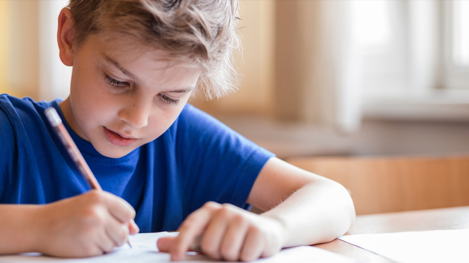 blonde haired boy writing inside a notebook using a pencil