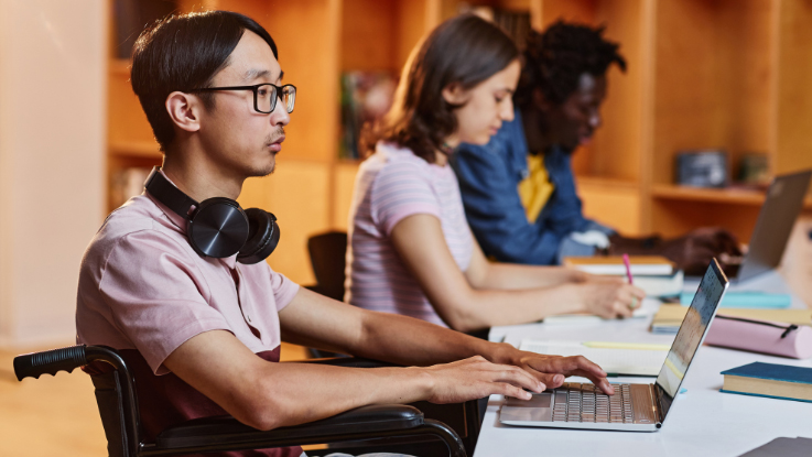 Student studying on a laptop in a classroom with peers, representing education support for young people.
