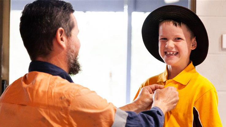 Adult helping a smiling school-aged child put on a school uniform shirt.