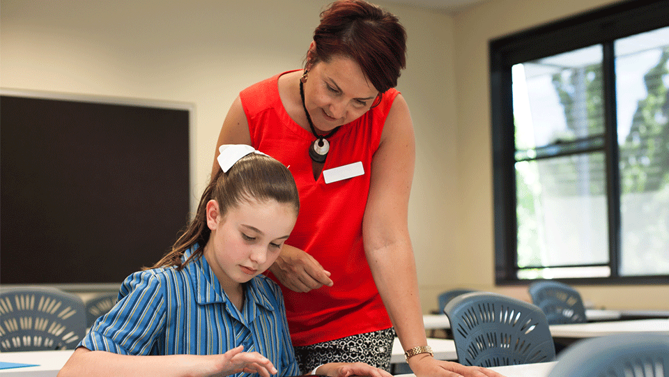 a school teacher wearing a red blouse is helping a school student with her work in the classroom